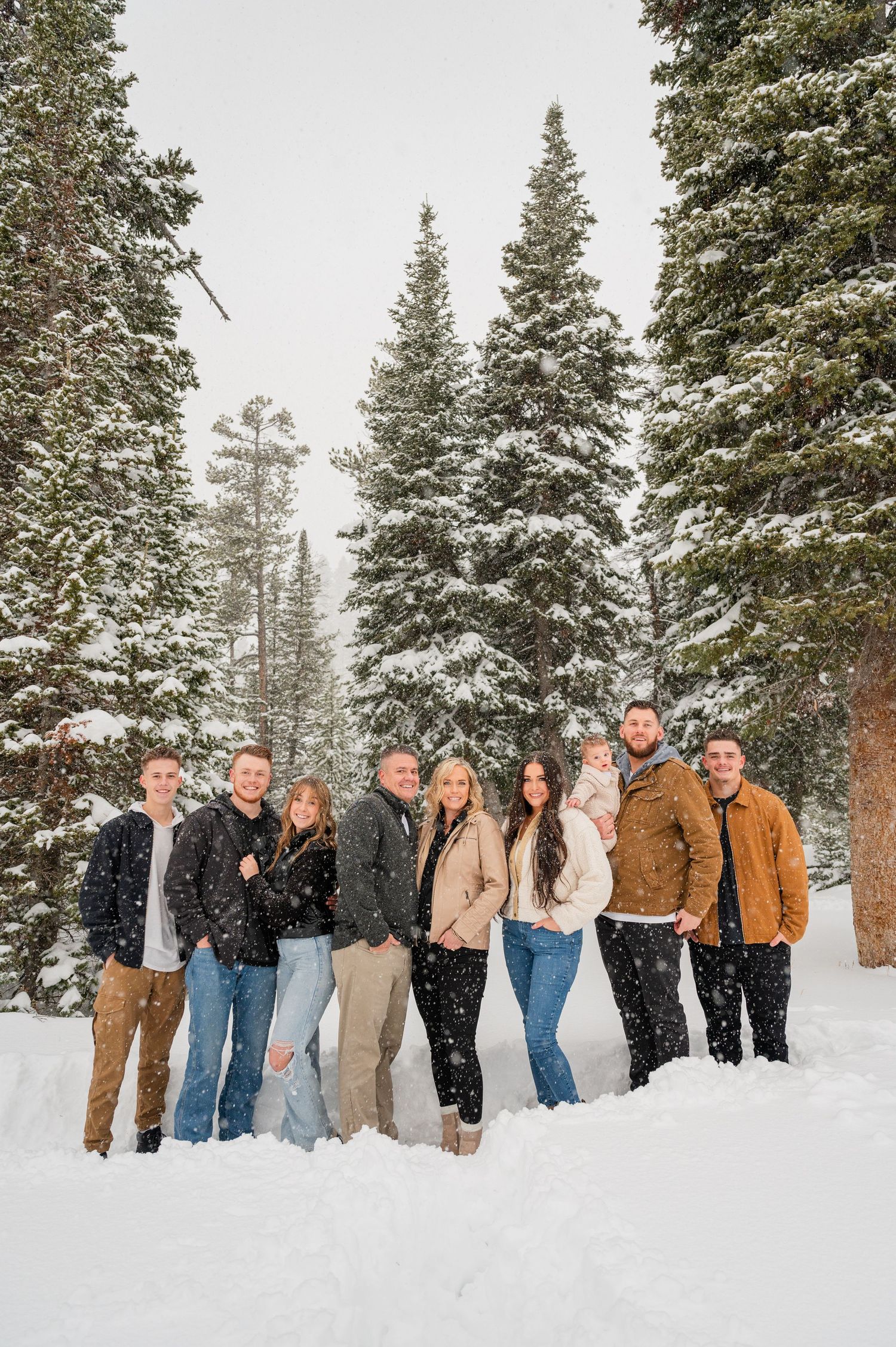 A group stands together in a snowy forest setting among tall evergreen trees.