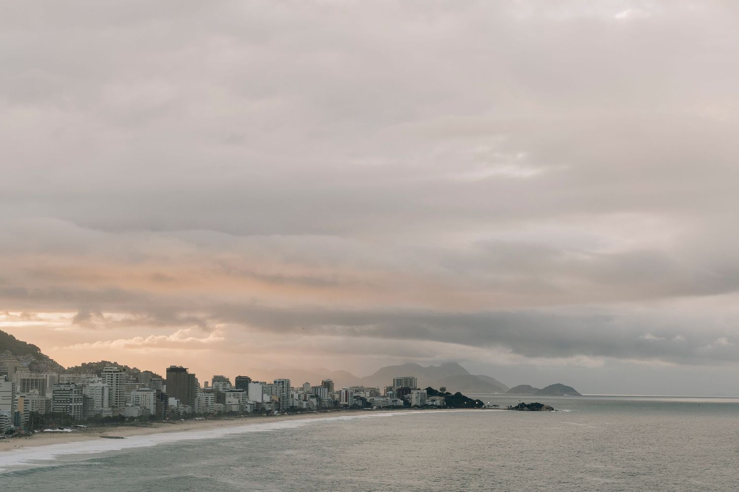 Overcast sky over Copacabana Beach coastline with city buildings and mountains in Rio de Janeiro, Brazil.