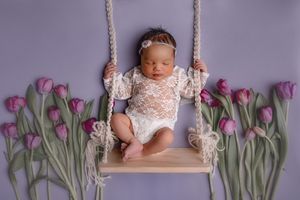 Newborn baby sitting on swing prop with tulips surrounding her in photo studio