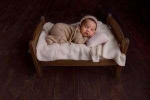 Newborn baby laying on tummy on tiny bed prop