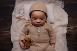 Baby laying on newborn bed prop holding deer plushy