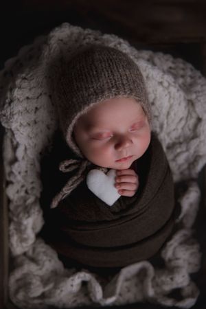 Newborn baby wrapped up in blanket holding felt heart inside basket