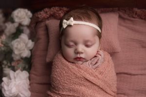 newborn baby wearing pink headband and swaddled in pink blanket close up picture