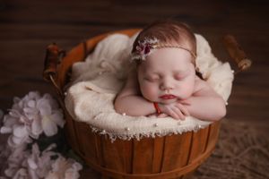 Newborn baby inside basket leaning on hands with chin
