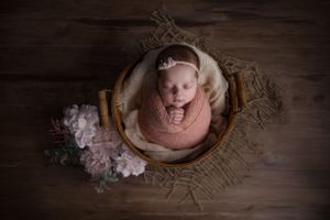 newborn baby swaddled inside basket with flowers around her