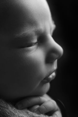 Black and white close-up portrait of a sleeping newborn baby with tiny hands tucked under chin.