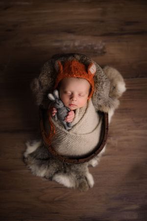 Newborn baby swaddled in wooden box with fox bonnet