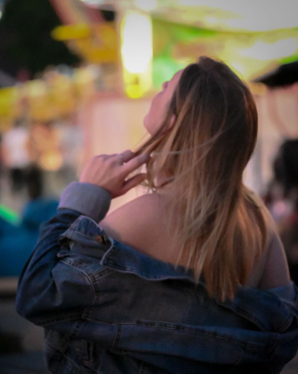 Back view of person with long hair wearing denim jacket in blurred setting.