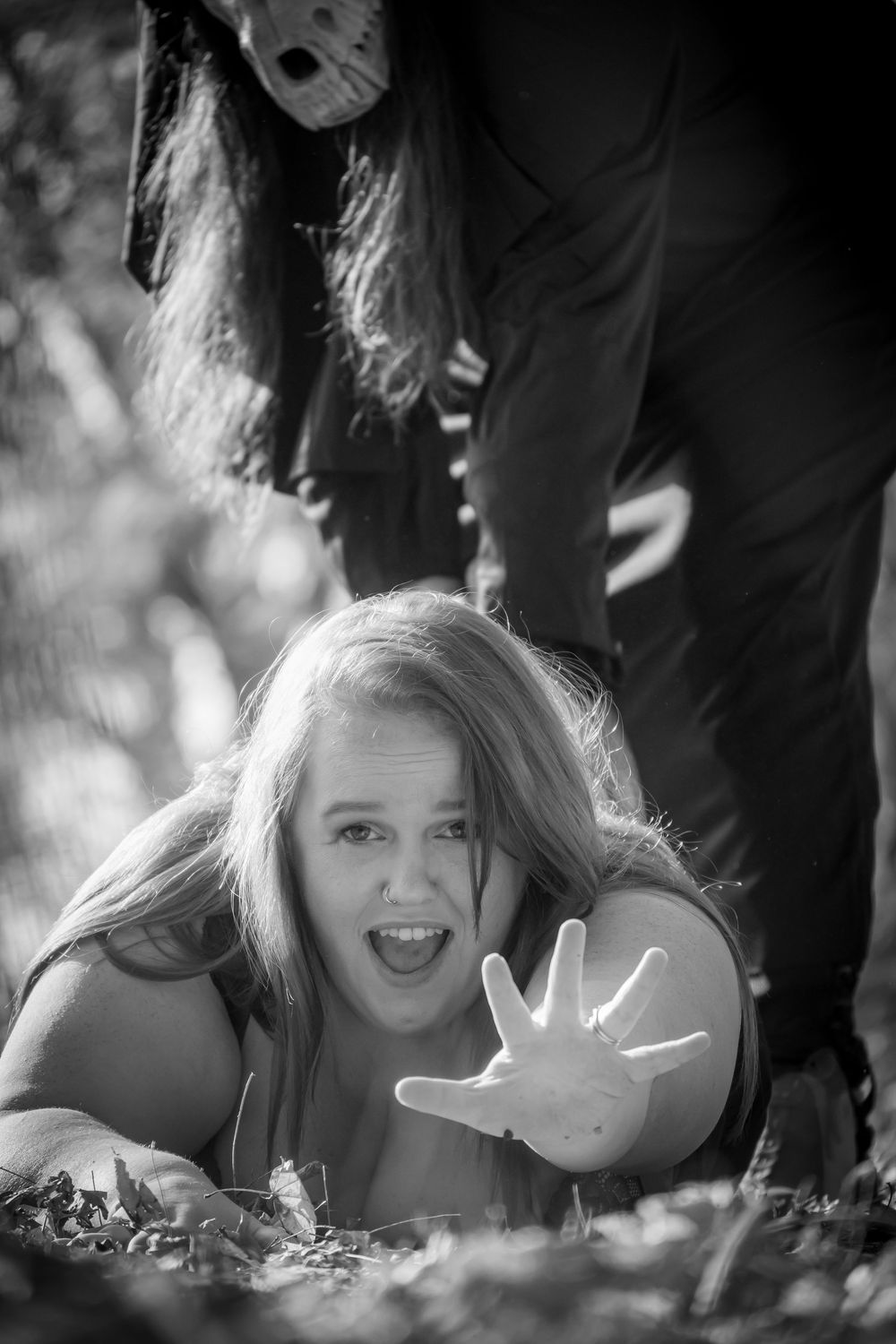 Creative black and white photo of person reaching out with open palm while lying in autumn leaves, with mysterious figure above.