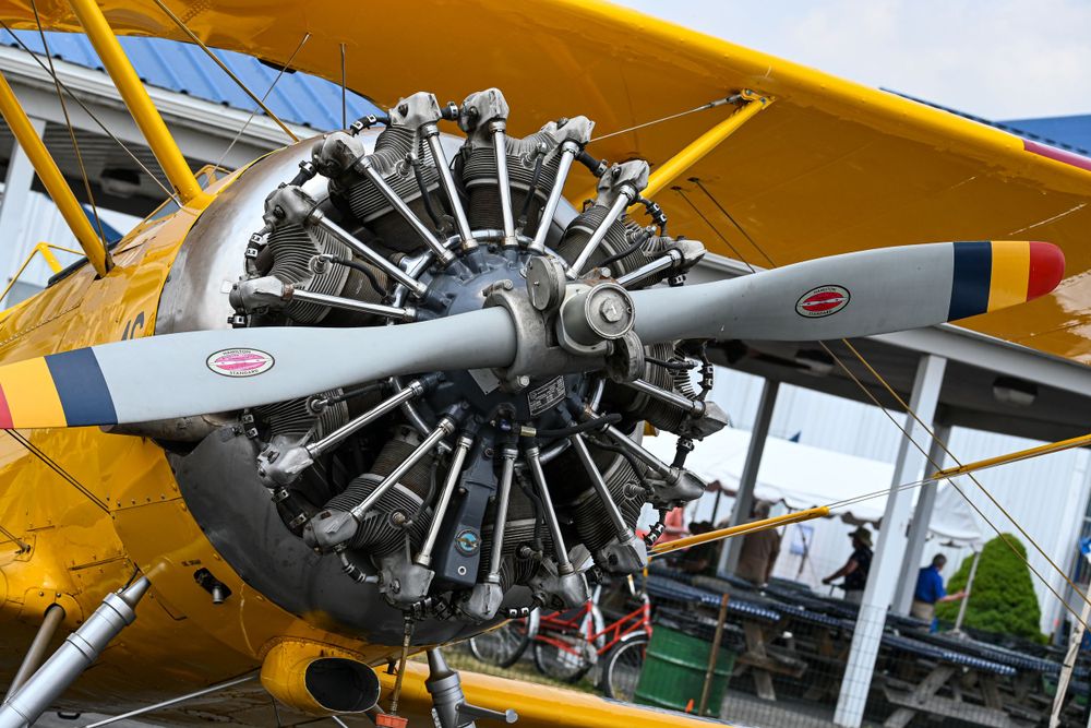 A vintage yellow biplane with radial engine on display at an outdoor aviation event.