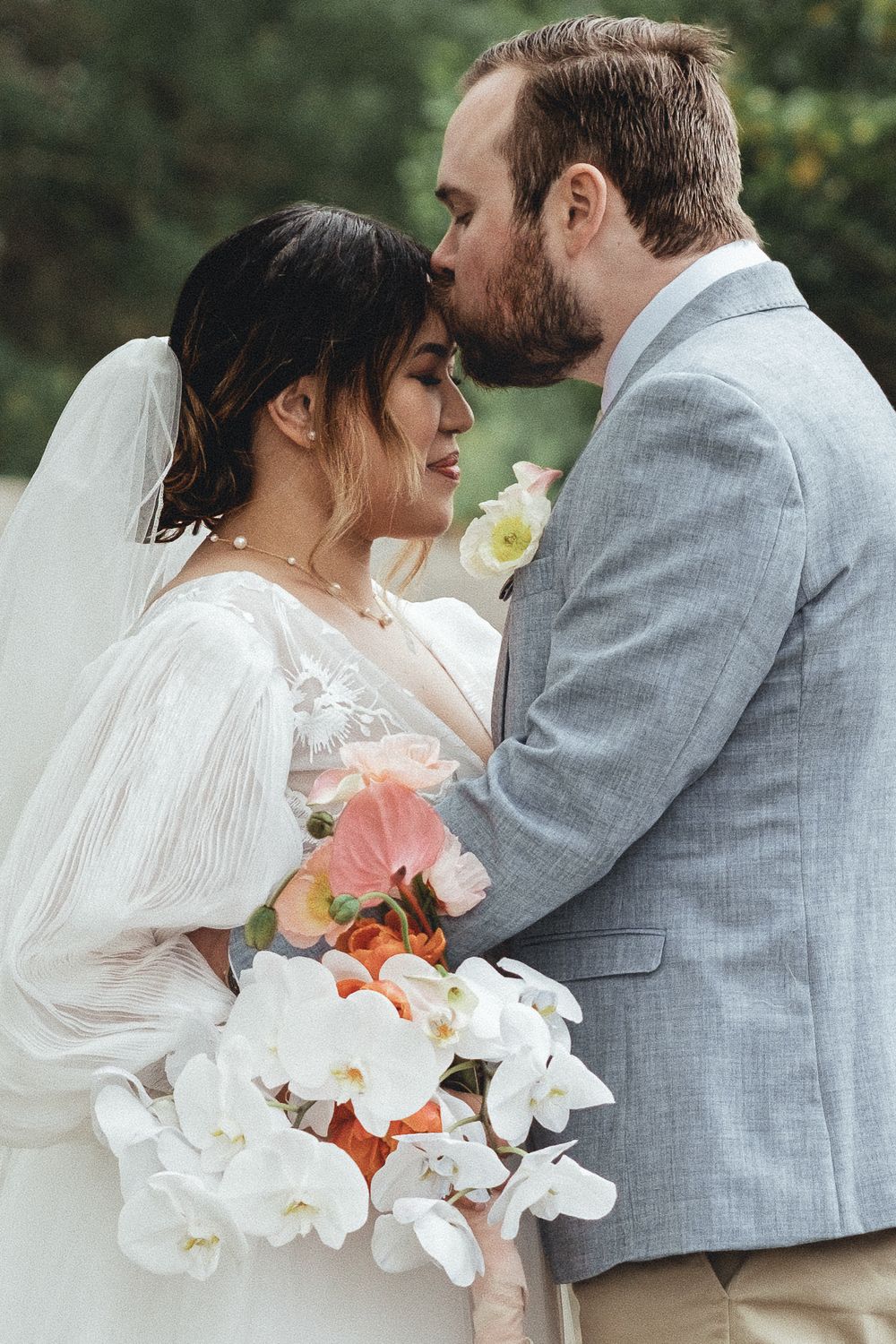 Intimate wedding moment with couple embracing outdoors with white orchid bouquet.