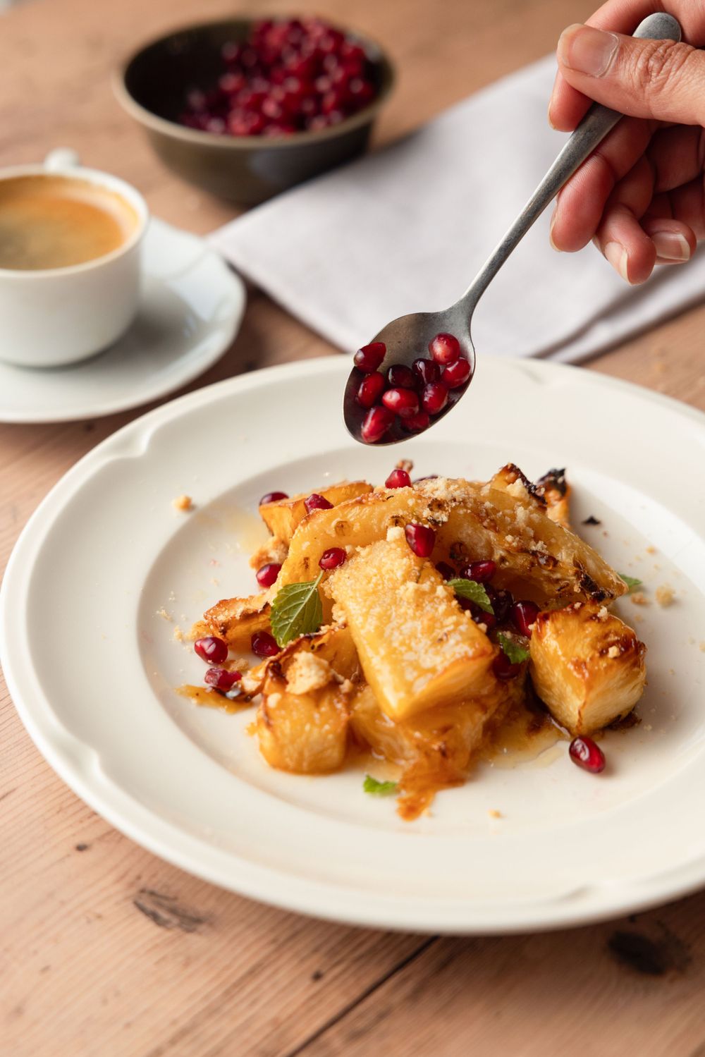 French toast garnished with pomegranate seeds and nuts served with coffee on a wooden table.