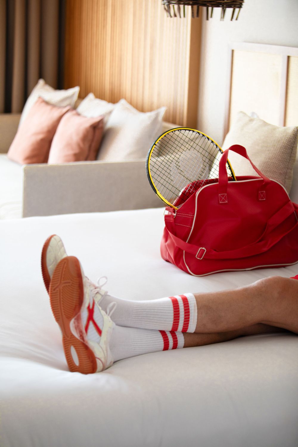 Tennis gear and red duffel bag on white hotel bed with striped athletic socks.