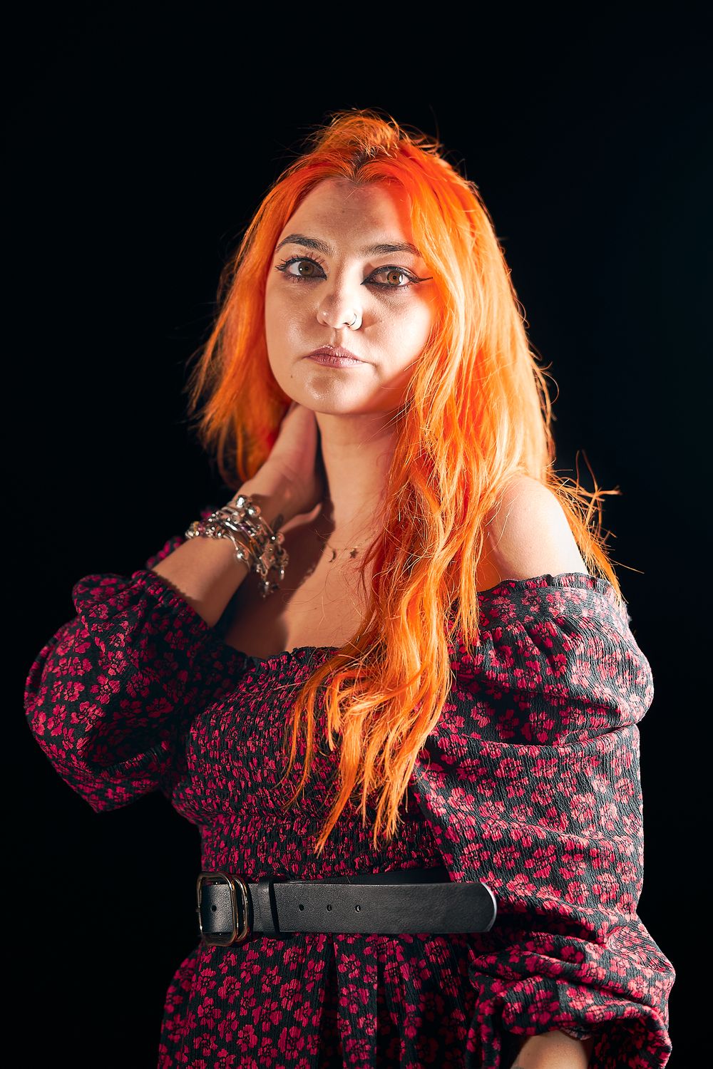 Studio portrait featuring vibrant orange hair and floral print dress against black background.