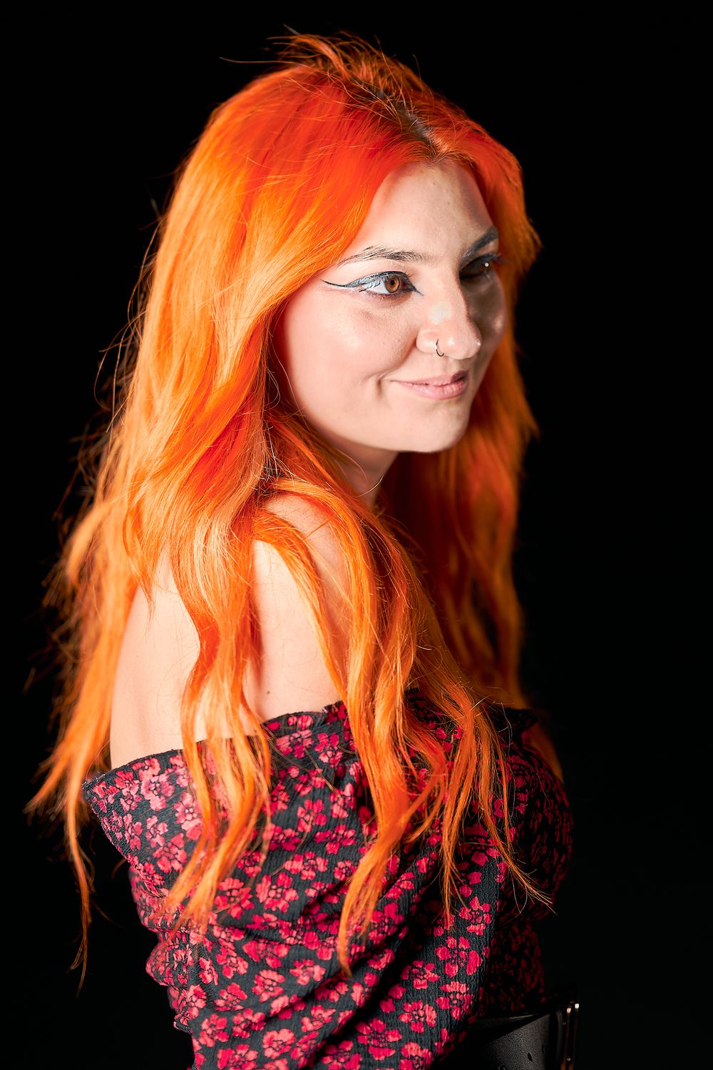 Bright orange hair contrasts with dark background in expressive studio portrait.
