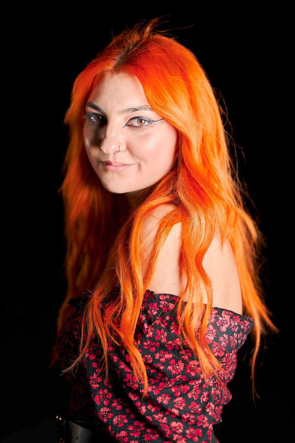 Portrait against black background featuring vibrant orange hair and floral dress with dramatic lighting.