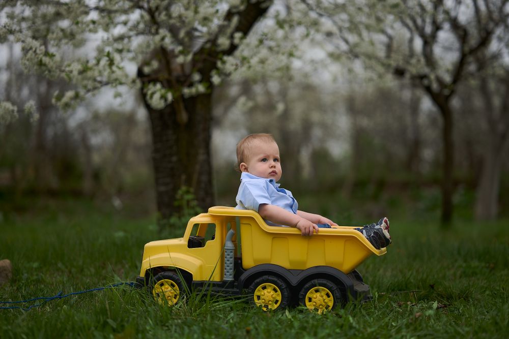 Child riding in yellow toy dump truck outdoors.