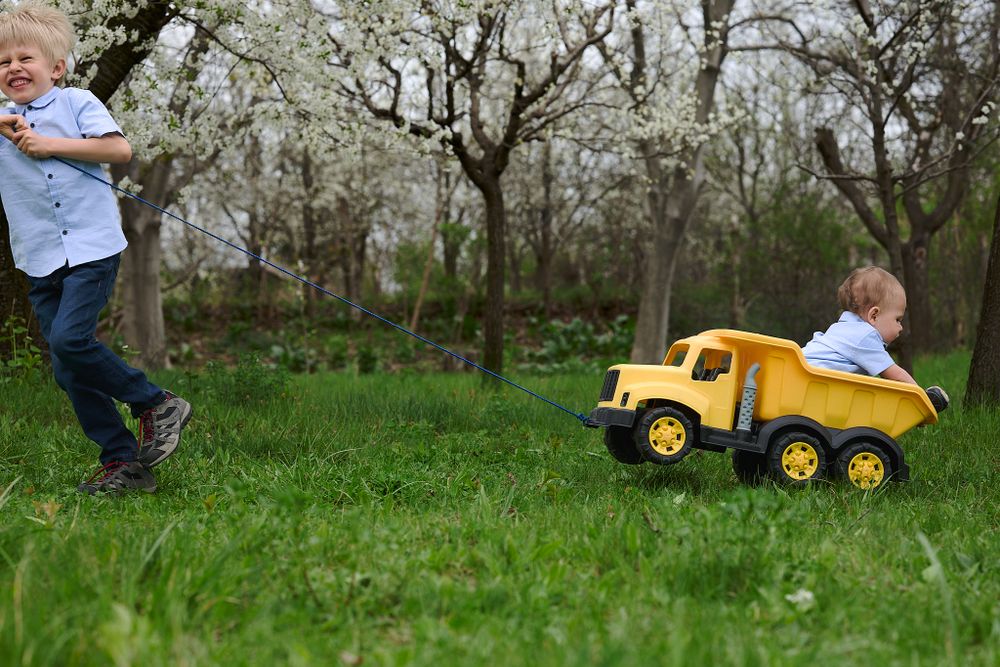 Child playing with large yellow toy truck in grassy field.