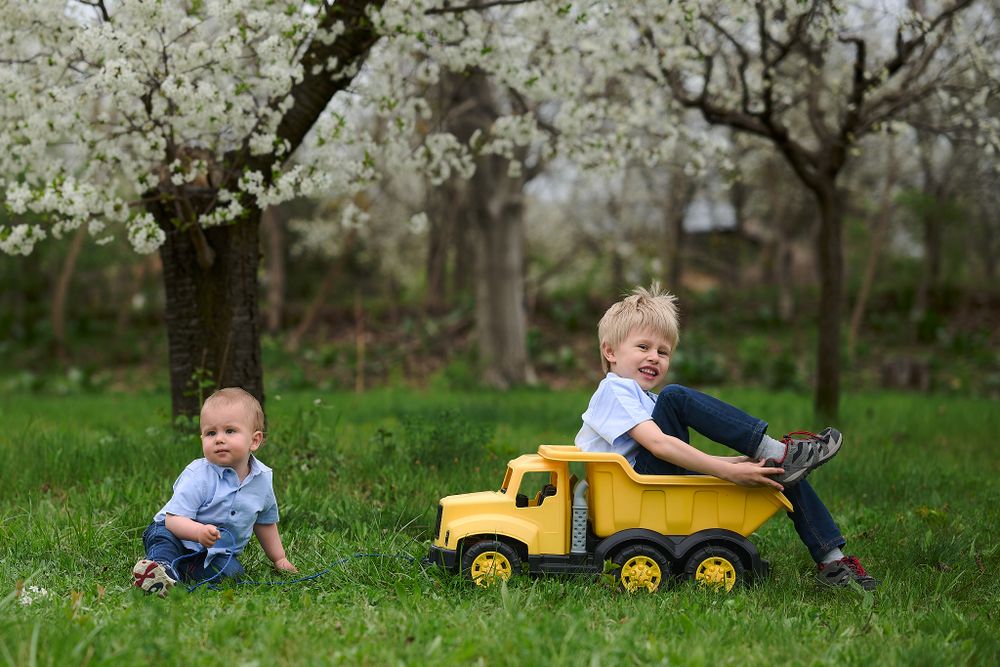 Children playing with a yellow toy truck in blooming orchard.
