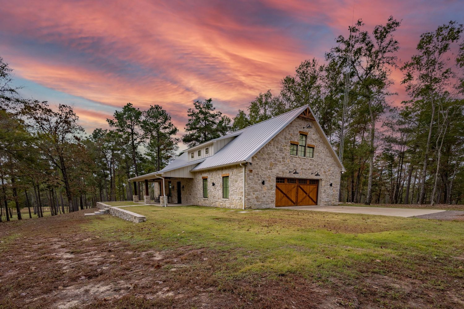 Elegant single-story stone home with two-car garage and manicured lawn under dramatic sunset sky.