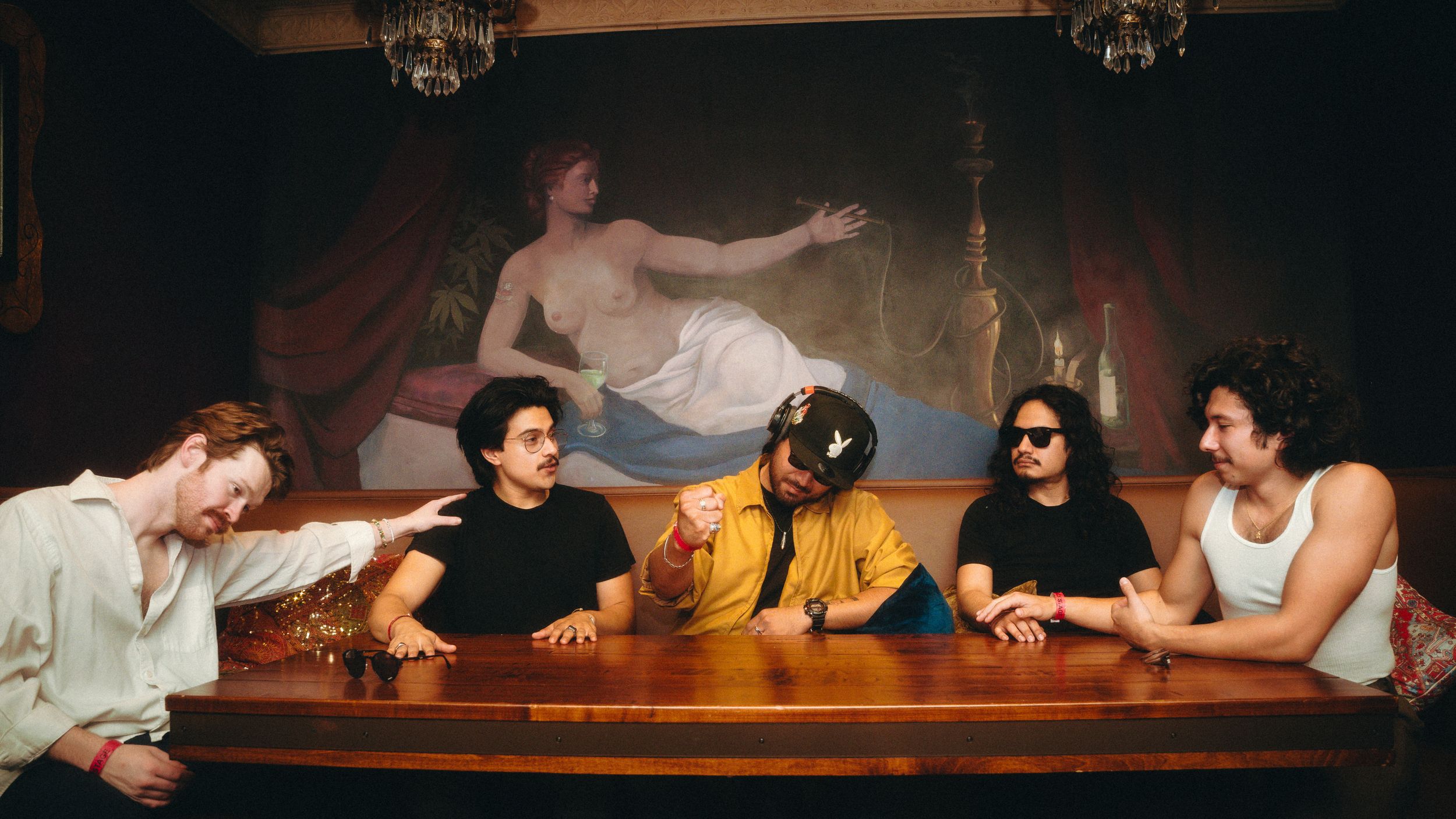 Five friends lounging together at a bar with a classical painting mounted on the dark wall behind them.