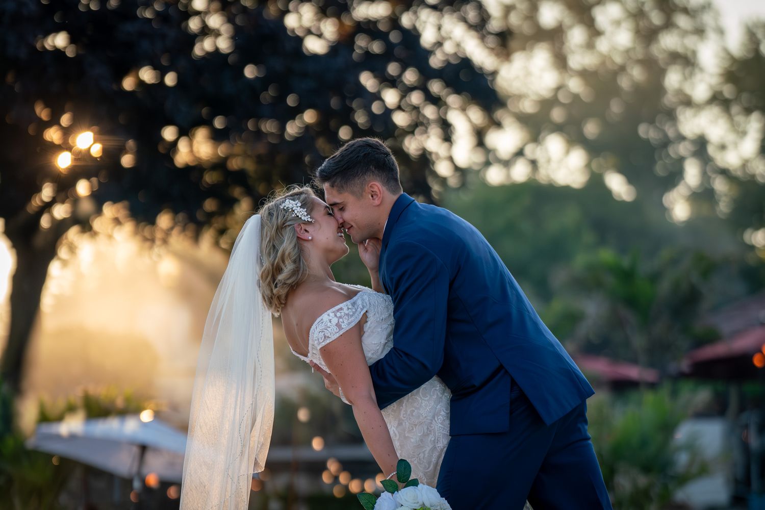 Sunset wedding portrait captured during golden hour with silhouetted trees in background.