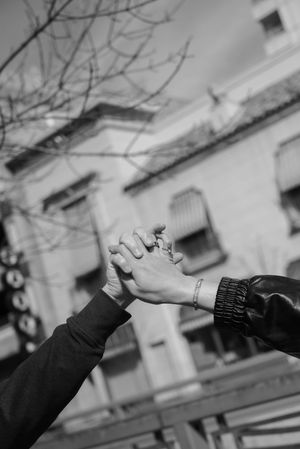 Black and white photo of two people holding hands outdoors with a building and bare tree in the background.
