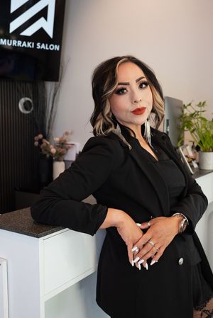 Woman in black blazer poses at Murraki Salon reception desk with styled hair and red lips.