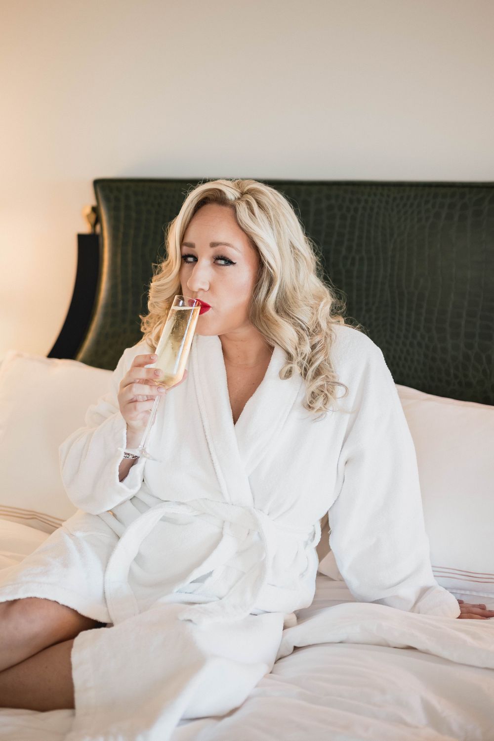 Relaxed scene showing someone in a white robe enjoying champagne in a luxurious hotel bed.