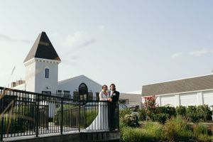 A couple poses for a wedding photo in front of a white chapel with a tower.