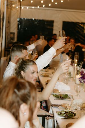 Wedding guests raising champagne glasses in toast during reception dinner.