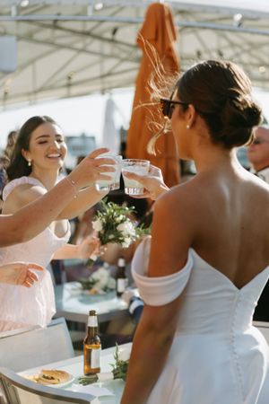 Wedding guests raise glasses in a celebratory toast with champagne outdoors on a sunny day.