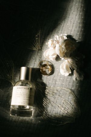 Artistic still life of perfume bottle, wedding rings and white flowers in dramatic lighting.