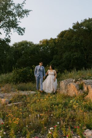 Couple walking hand in hand through wildflower meadow during sunset wedding photoshoot.