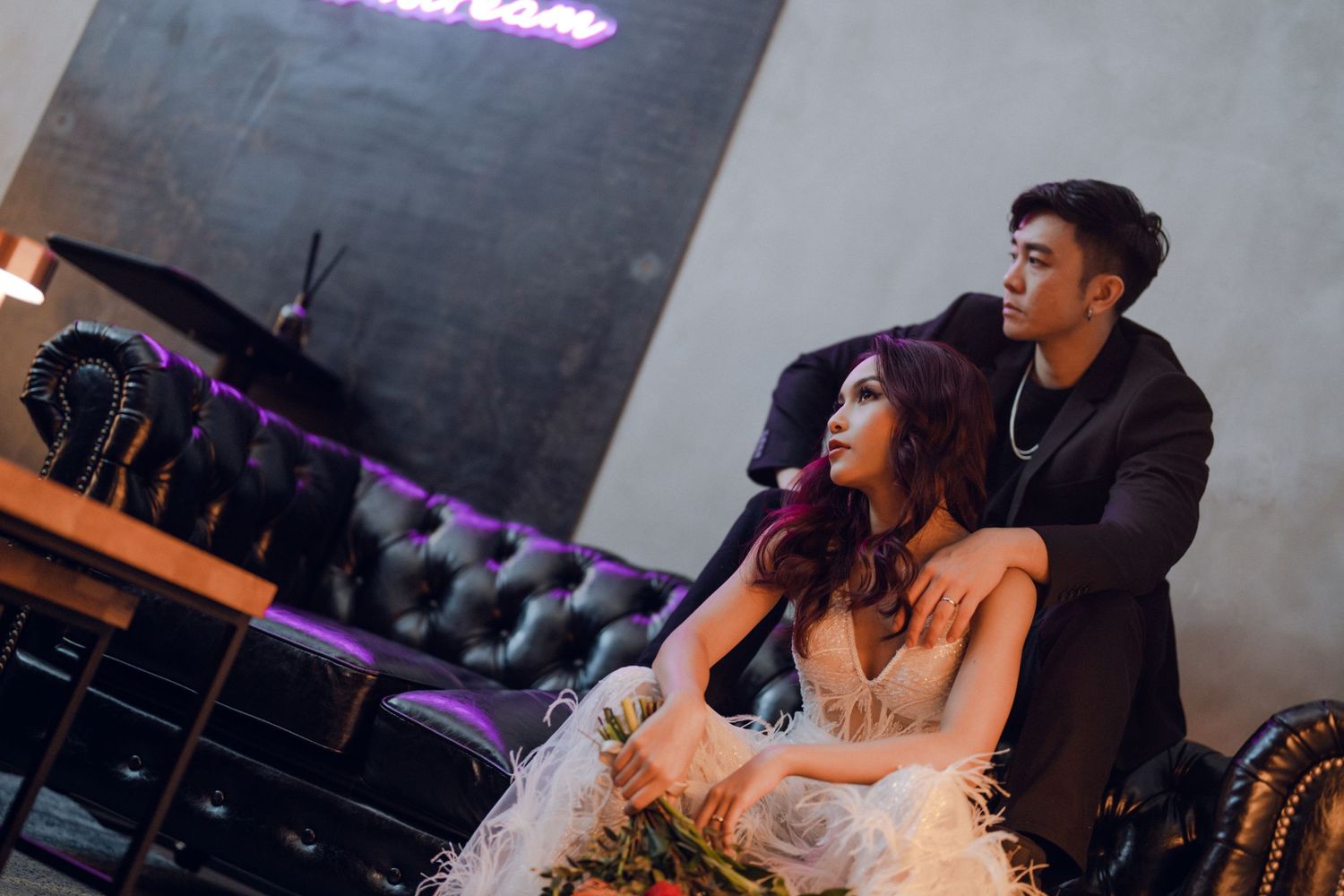 Romantic couple in formal wear sharing intimate moment under purple neon lights.