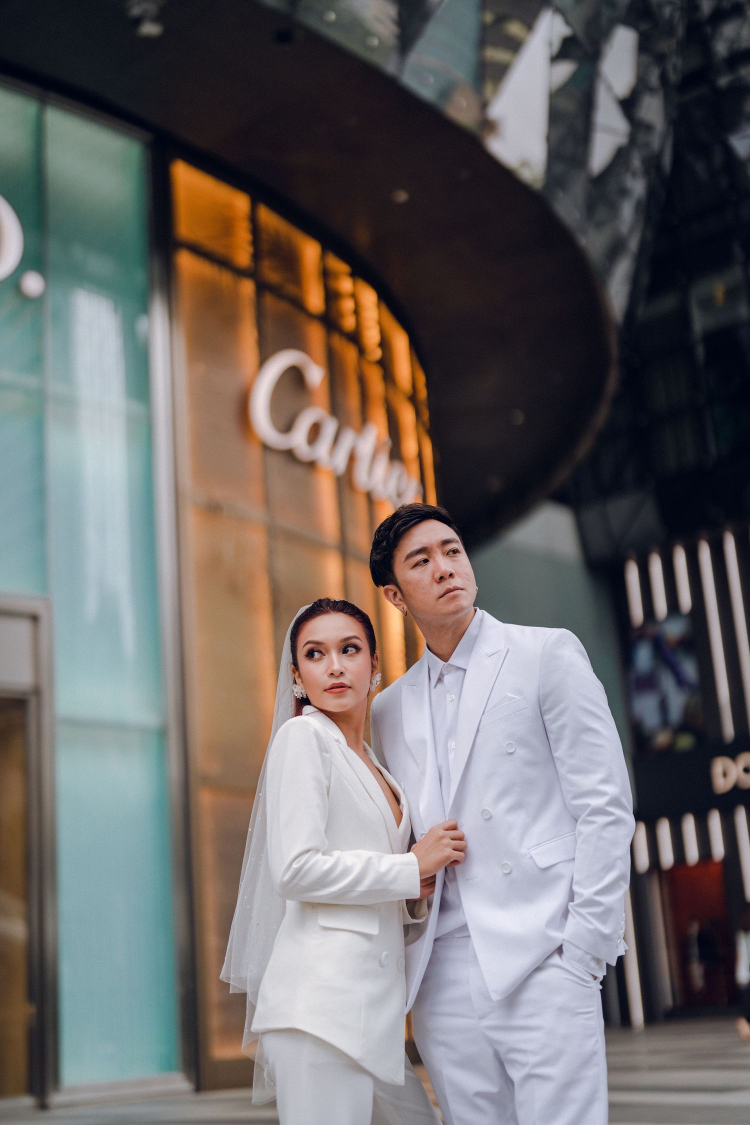 Stylish couple in white outfits sharing a moment outside luxury retail store.