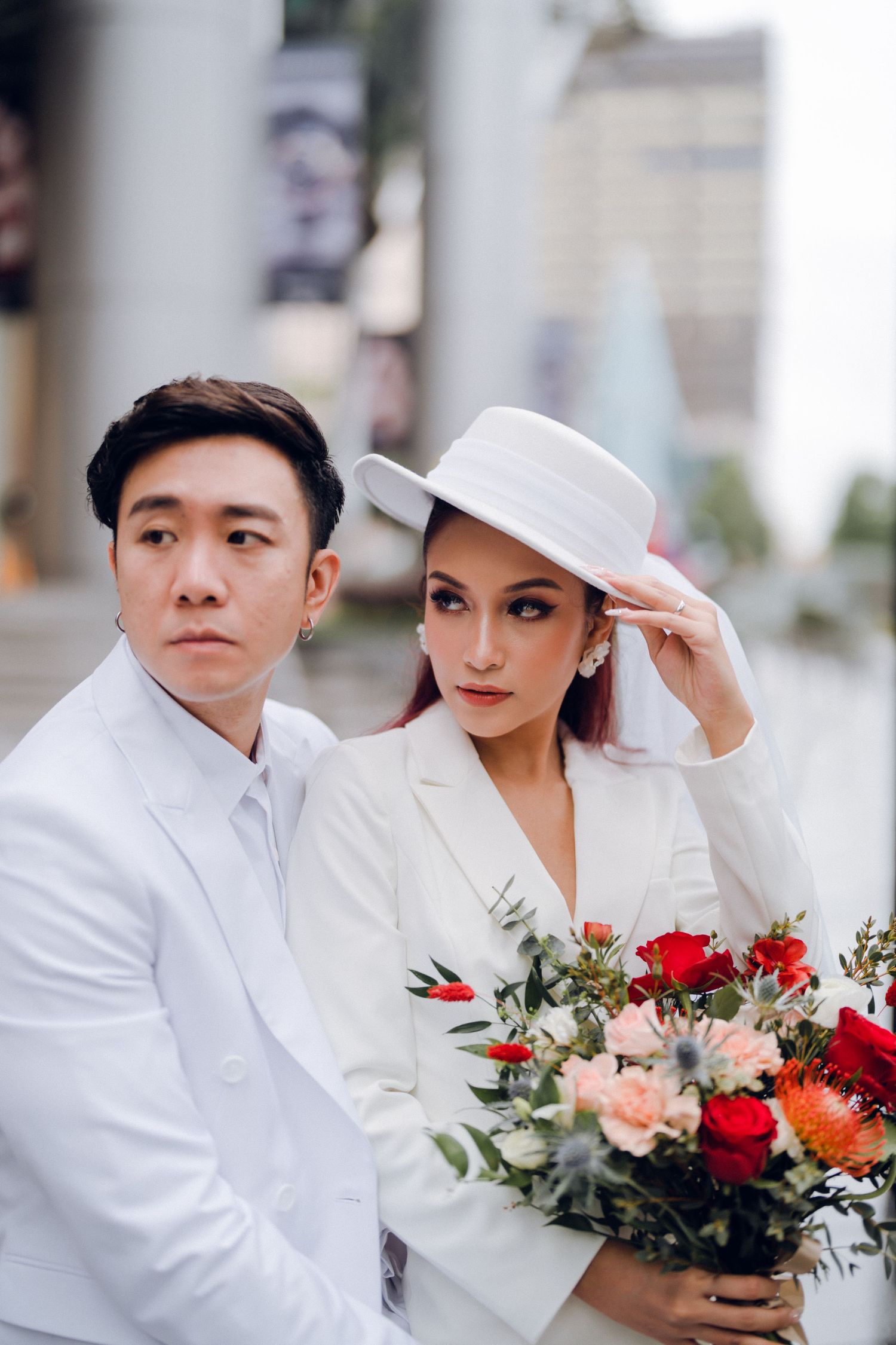 Romantic couple in white attire poses with floral bouquet.