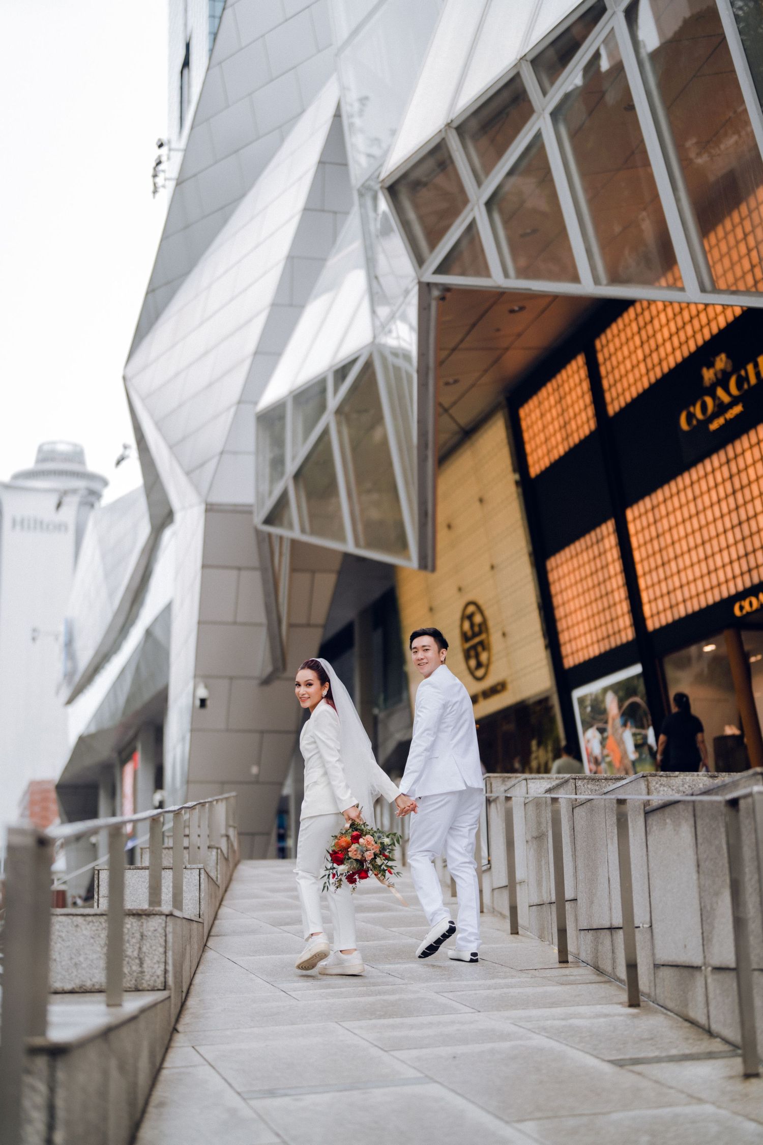 A couple in white outfits walking together in a modern architectural space with geometric patterns.