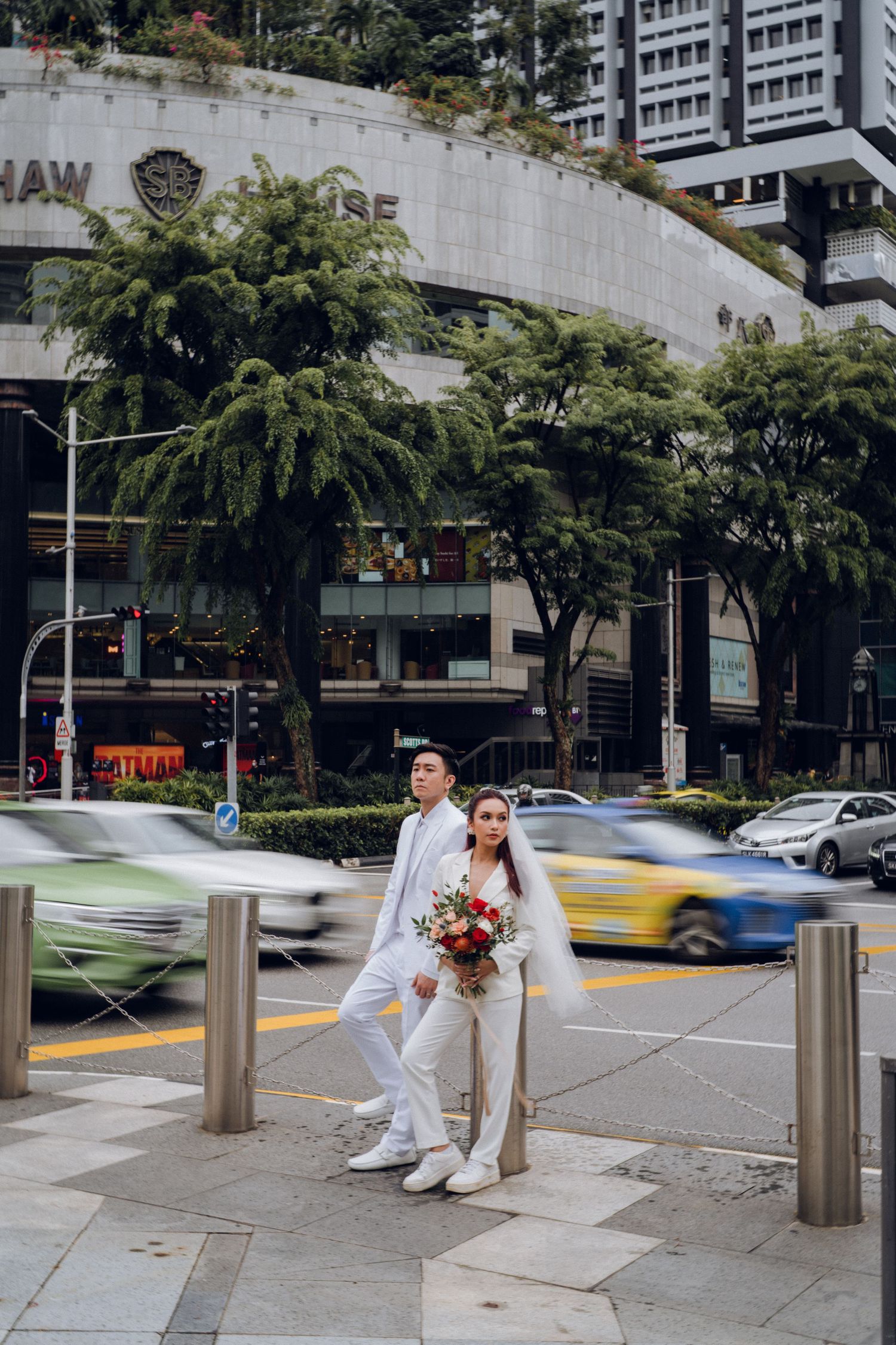 A couple in white clothing sitting on urban bollards with cars and buildings in the background.