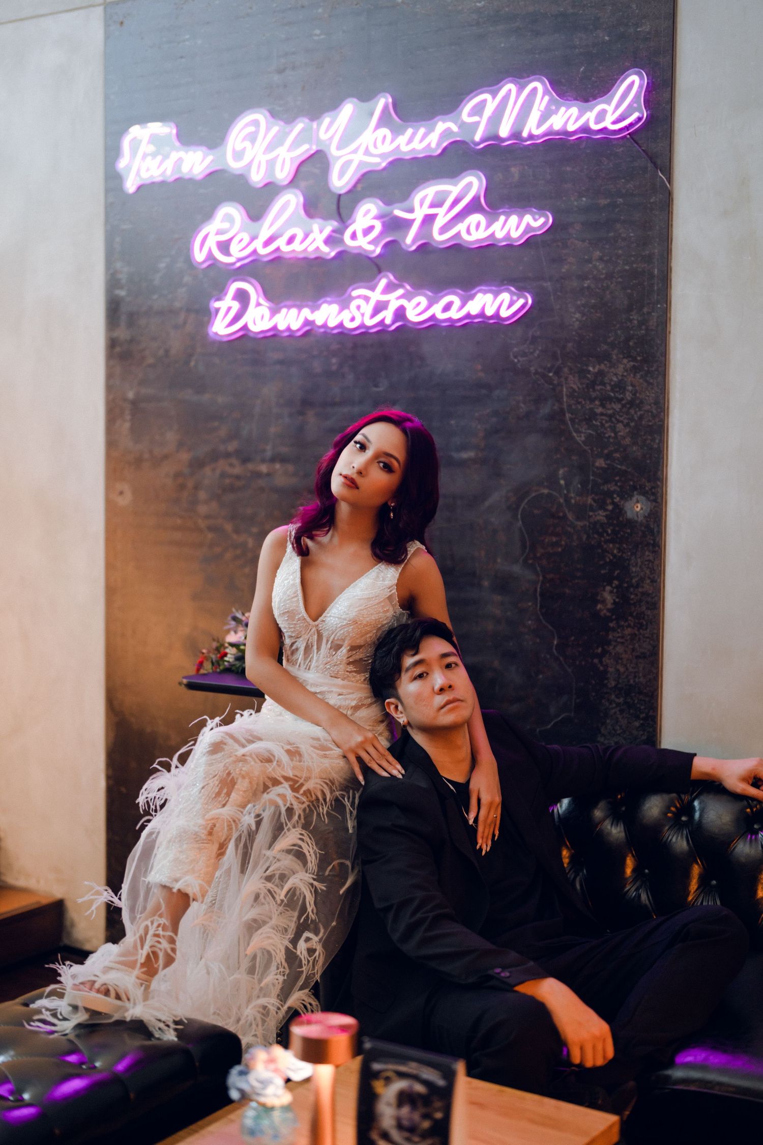 Romantic couple lounging on black couch under purple neon lights.