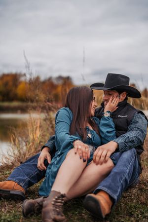 A couple relaxes intimately together on autumn grass near a lake during a romantic outdoor photoshoot.