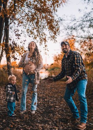 Family enjoying a playful autumn moment together on a leaf-covered trail surrounded by orange fall foliage.