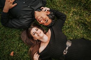 Person in black clothing lying on green grass with eyes closed in a peaceful pose.
