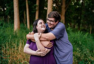 A couple embraces lovingly in a lush green forest setting during a romantic outdoor photoshoot.