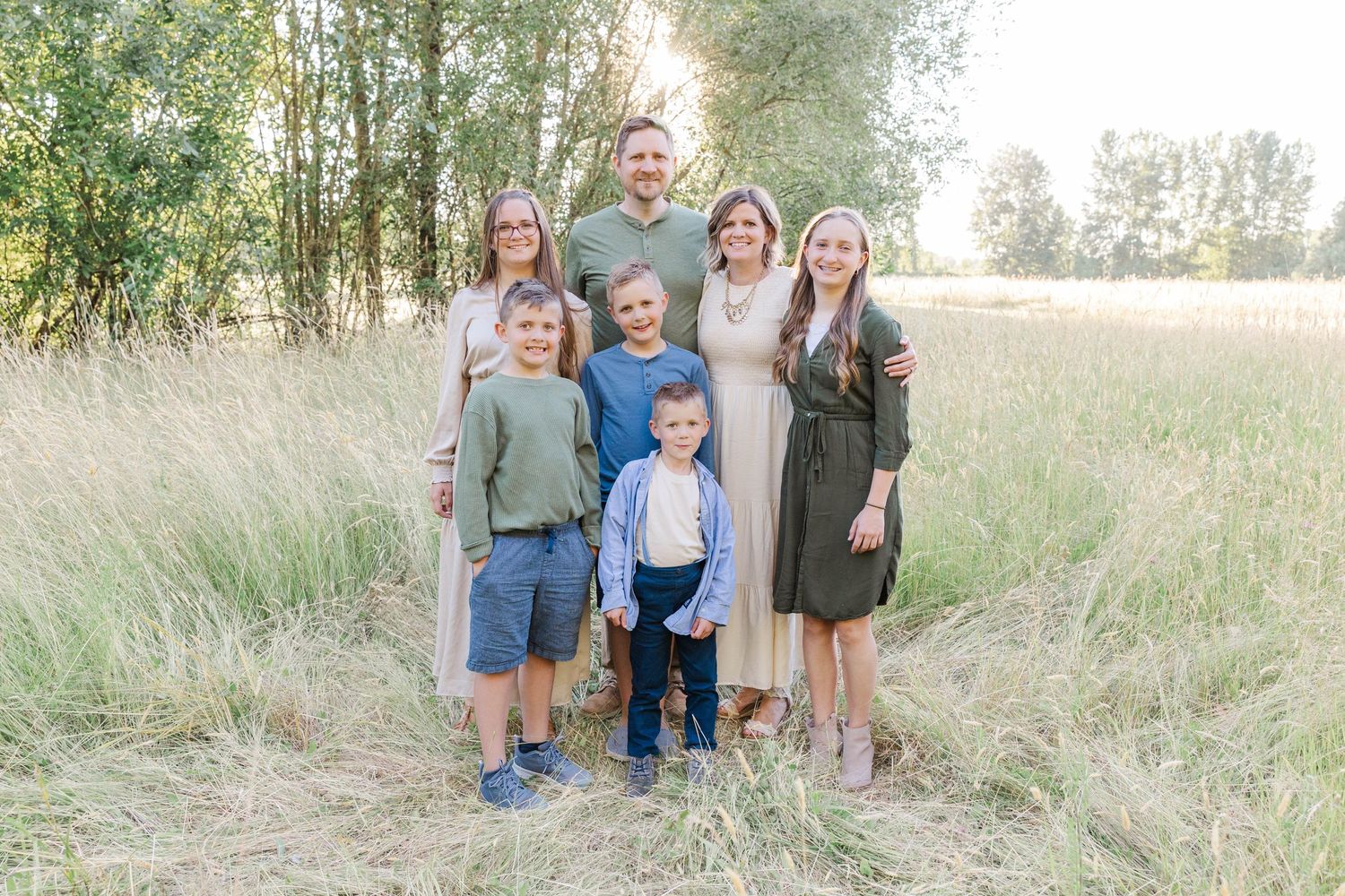Family of seven posing together in a sunlit field of tall golden grass at sunset.