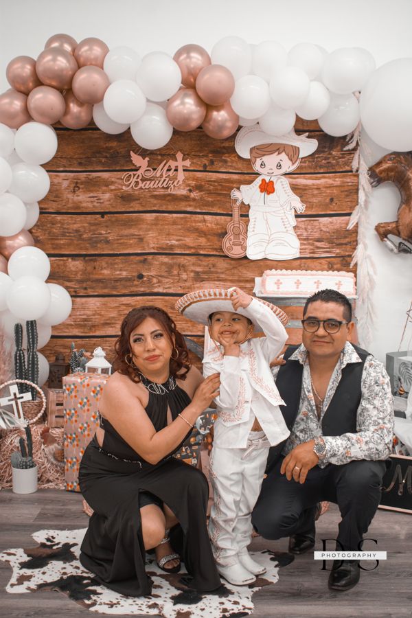Family celebration with rose gold and white balloon arch against rustic wooden backdrop.