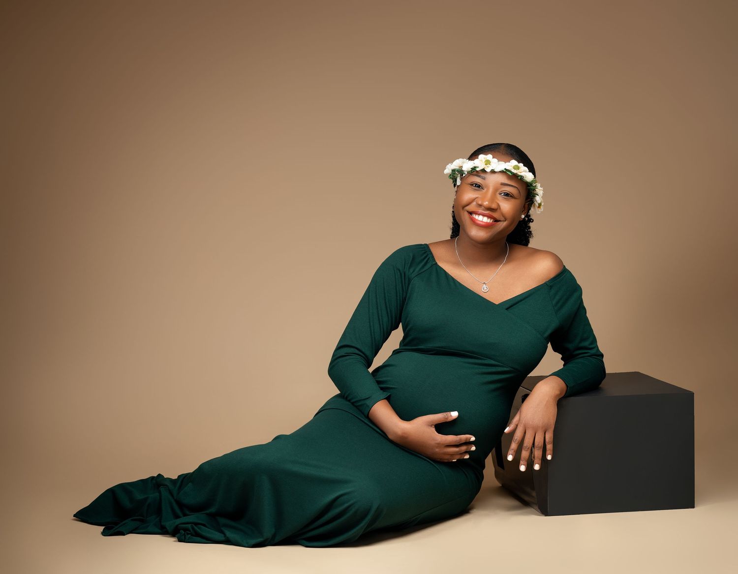 Maternity portrait in emerald green dress against neutral backdrop.