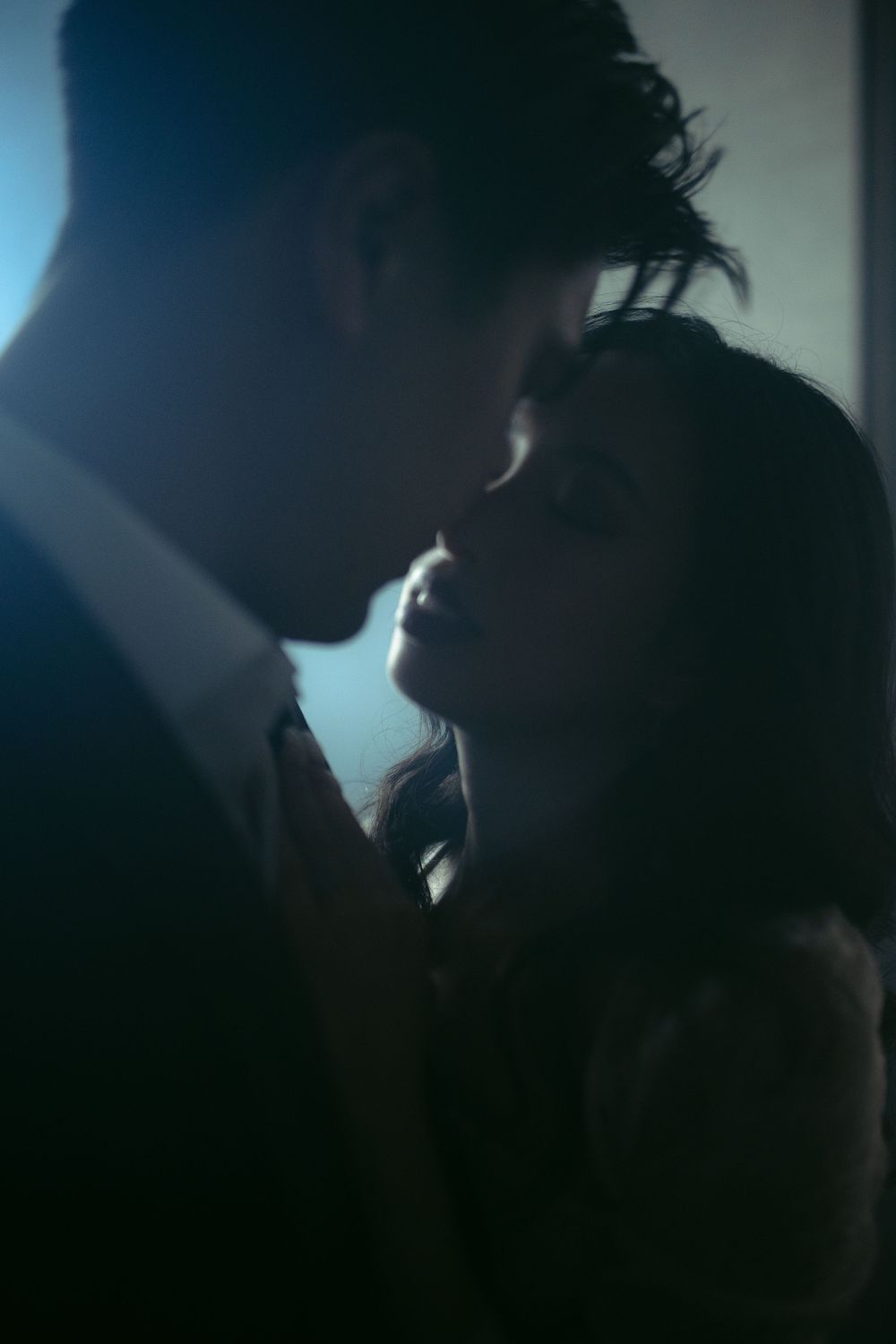 Silhouetted couple in a tender embrace against moody blue lighting.