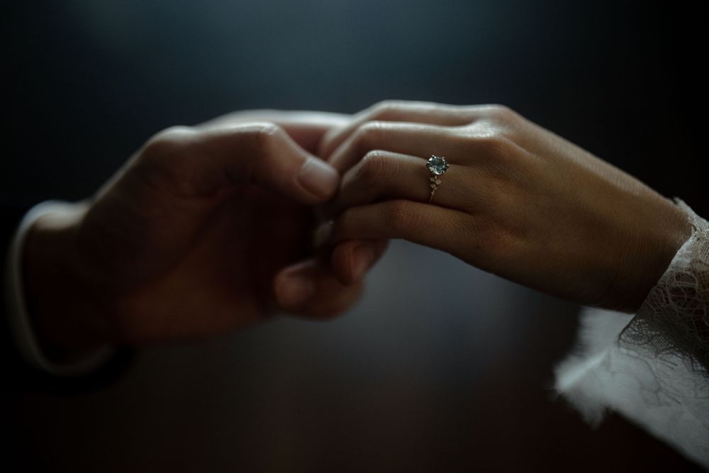 Detailed shot of hands touching with engagement ring visible in dim lighting.