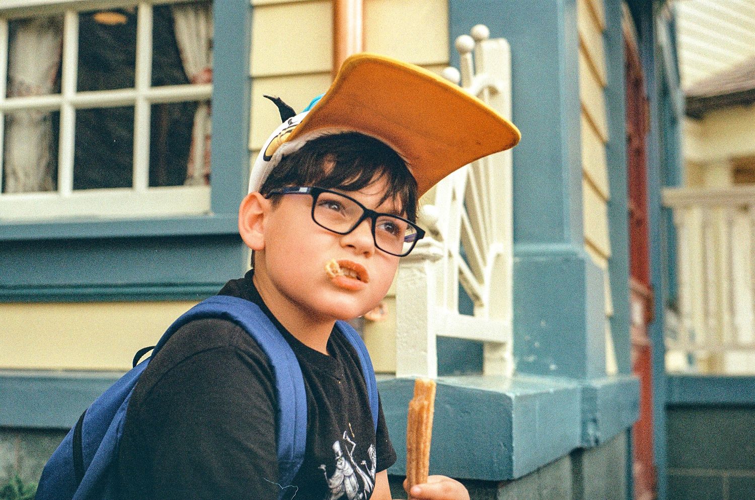 Young tourist in an orange hat and backpack poses against a blue building.